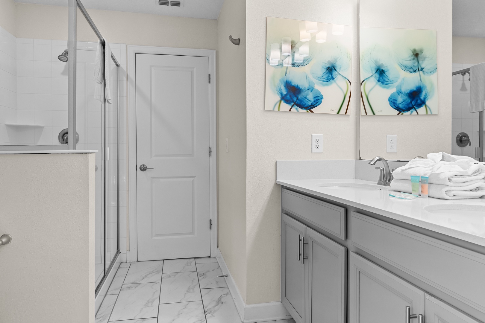 Your stylish bathroom features a spacious walk-in shower, modern gray vanity, and soothing blue artwork to start your mornings refreshed.