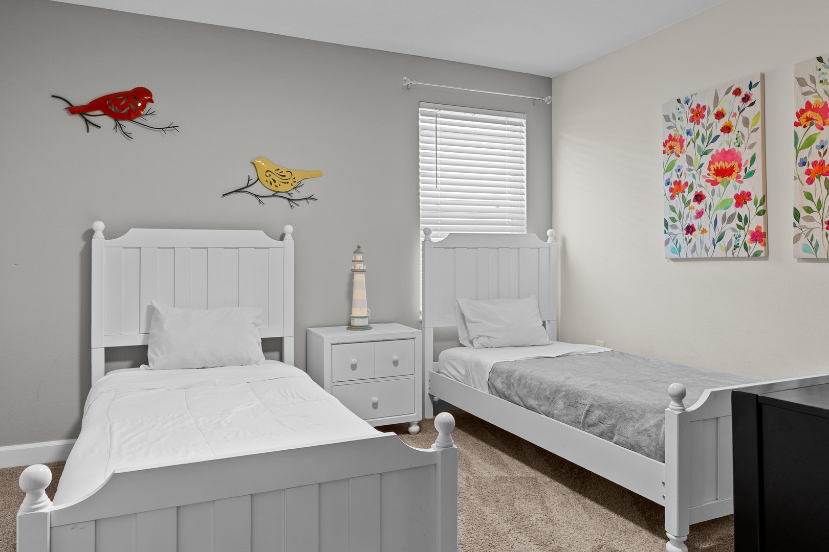 Sweet dreams await in this cheerful twin bedroom with playful bird art and bright floral paintings creating a welcoming space.