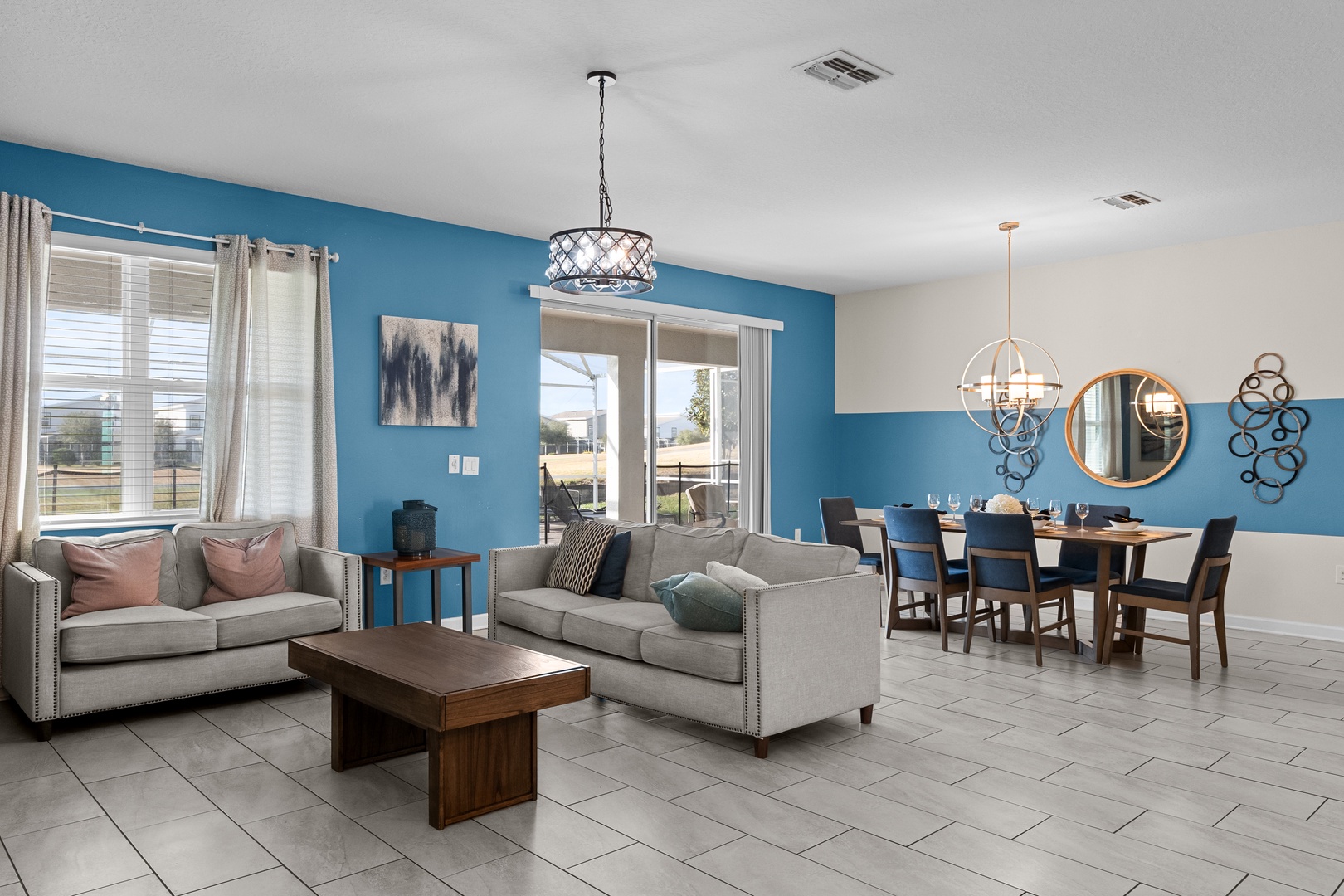 Relax in your spacious open-concept living space featuring modern furnishings, vibrant blue accent walls, and elegant pendant lighting.