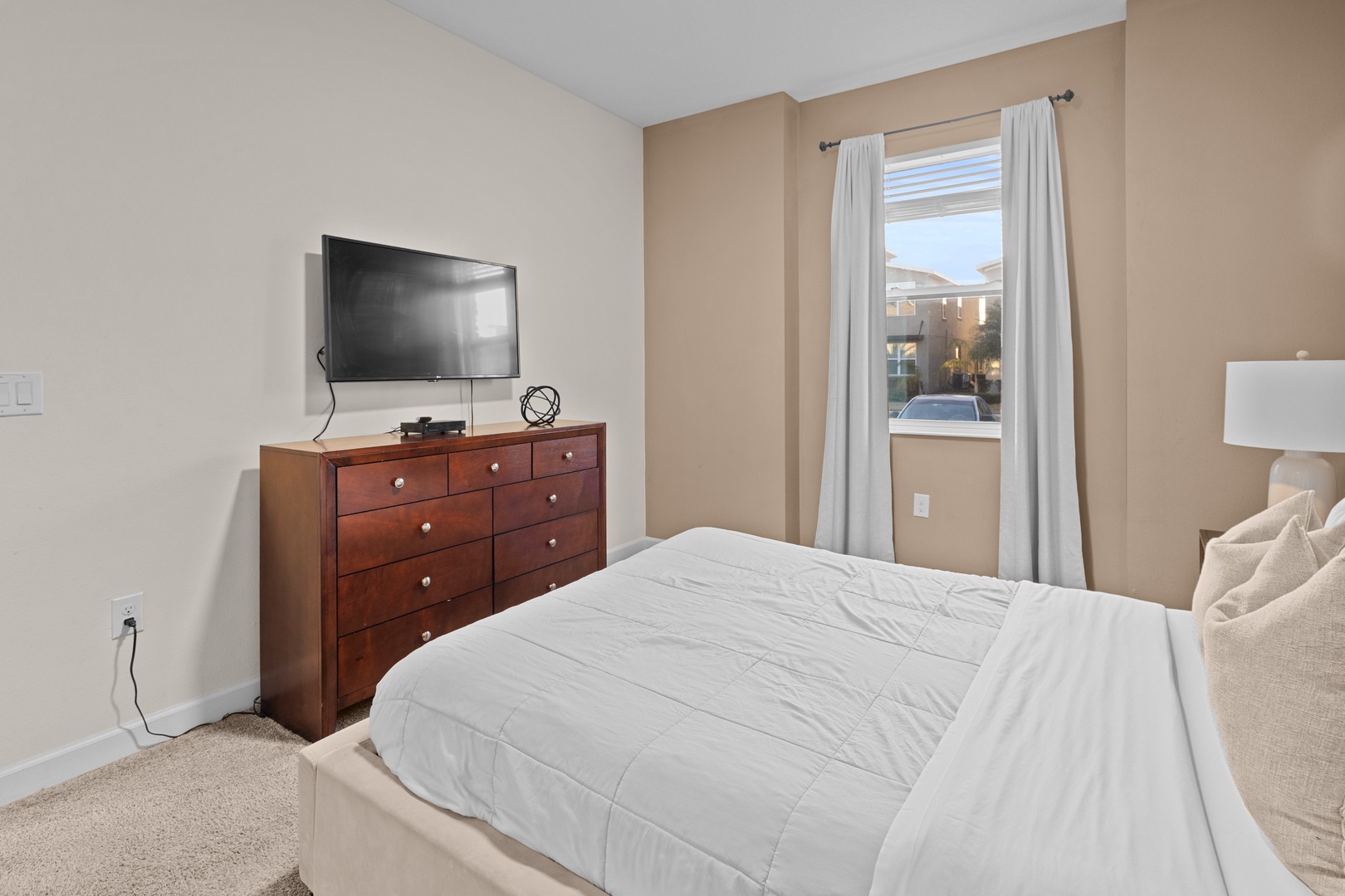 Unwind in your peaceful bedroom with plush bedding, wall-mounted TV, and ample storage in the rich wooden dresser.