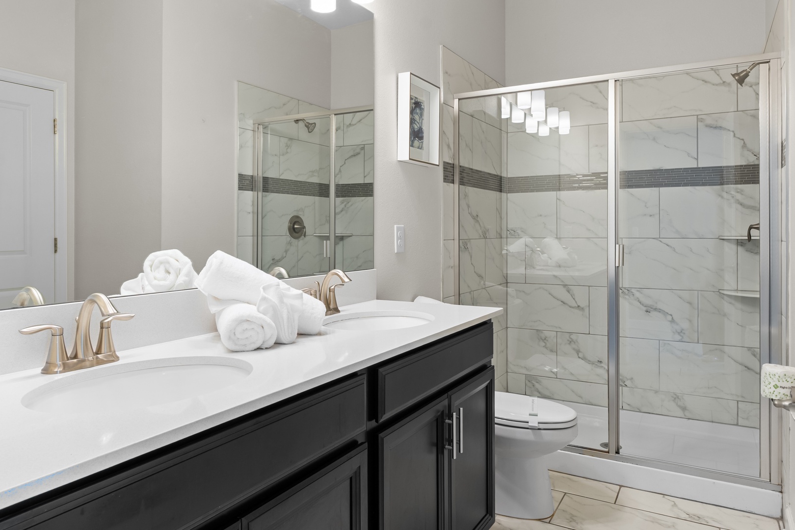 Indulge in your luxurious marble bathroom featuring a spacious glass shower, dual vanities, and plush towels waiting for your arrival.