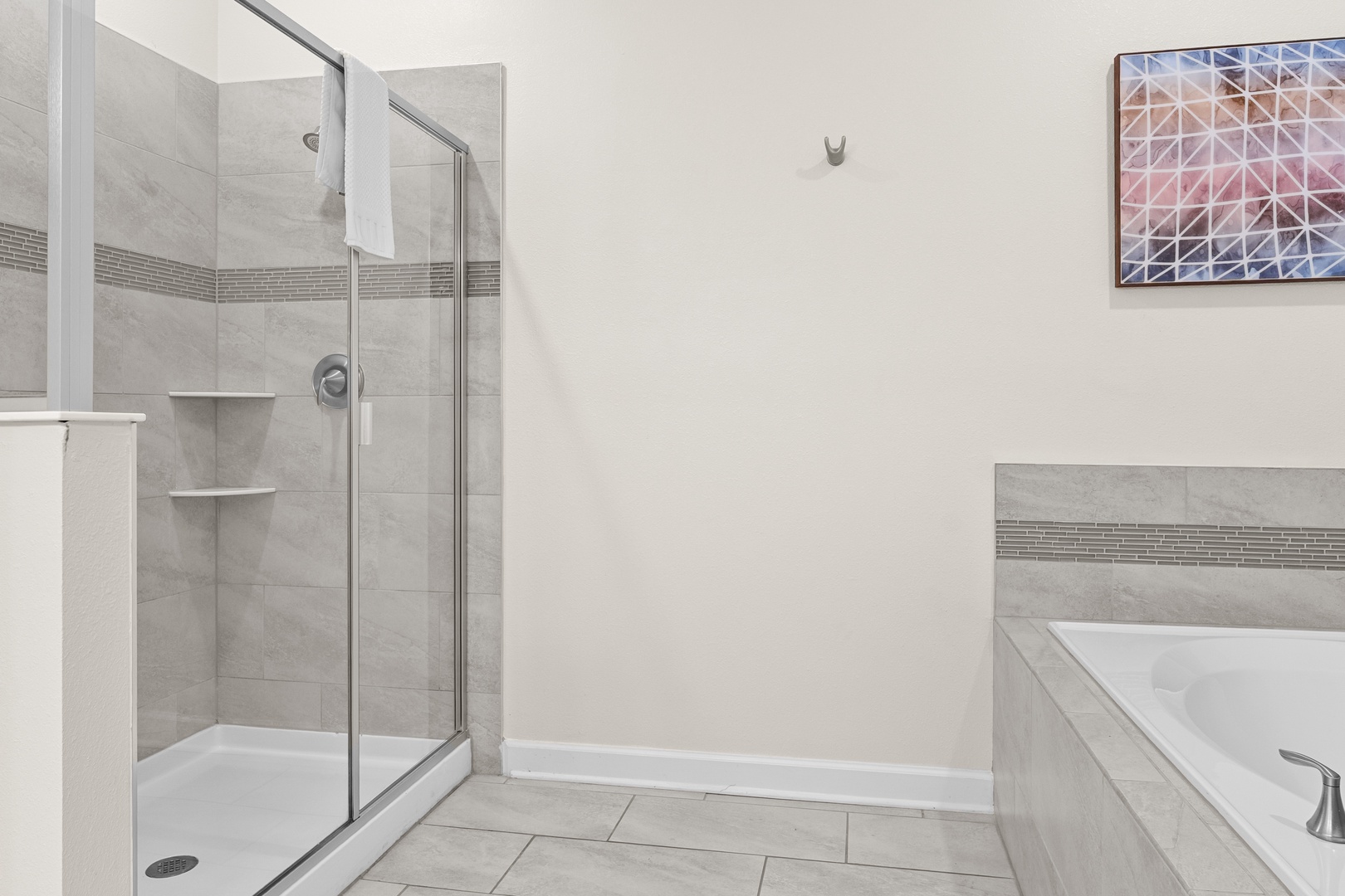 Unwind in your private spa-like bathroom with elegant gray tiling, spacious glass shower, and relaxing soaking tub.