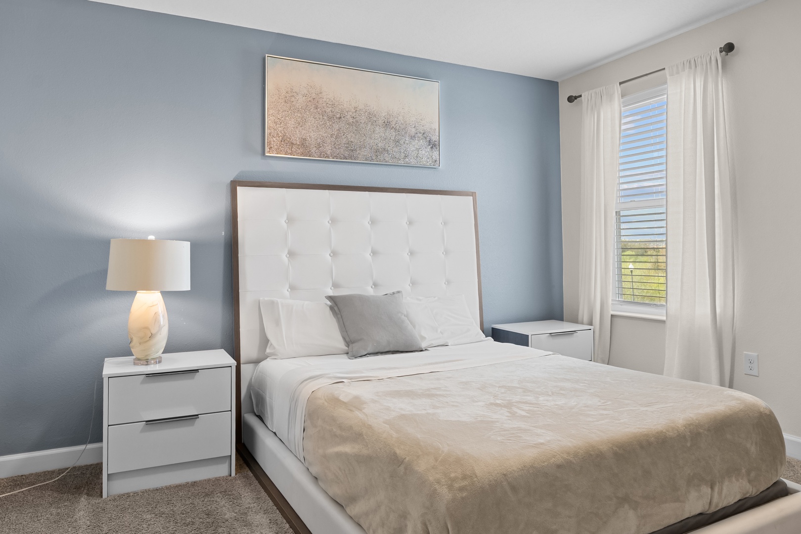 Drift off to sleep in your peaceful bedroom with plush bedding and natural light streaming through crisp white curtains.