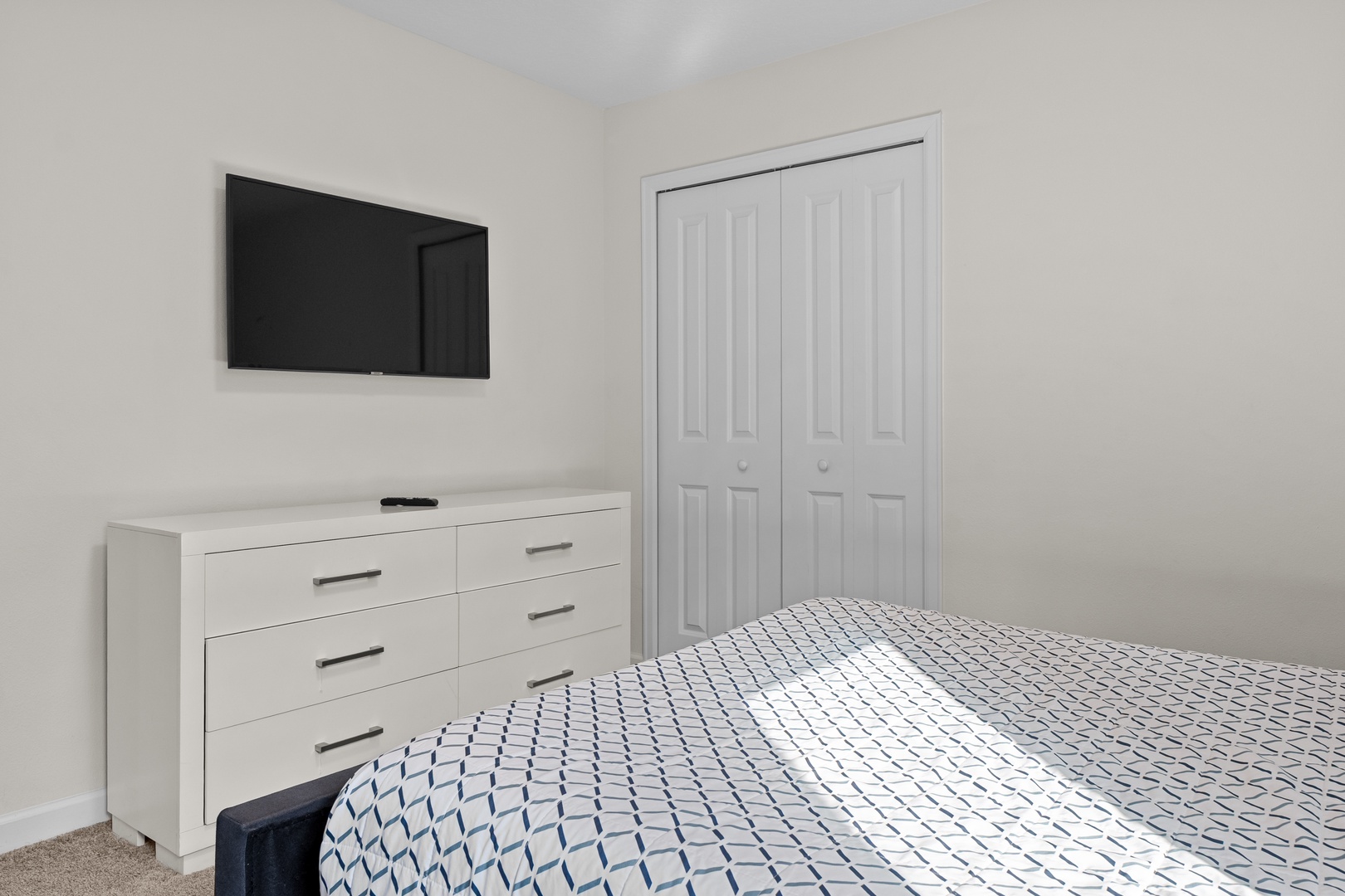 Your peaceful bedroom features a comfortable bed, modern dresser, wall-mounted TV for entertainment, and ample closet storage.