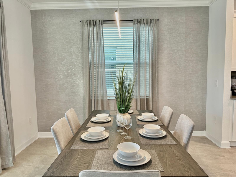 Gather around this elegant dining table for memorable meals with your group, featuring stylish place settings and natural light streaming through soft curtains.