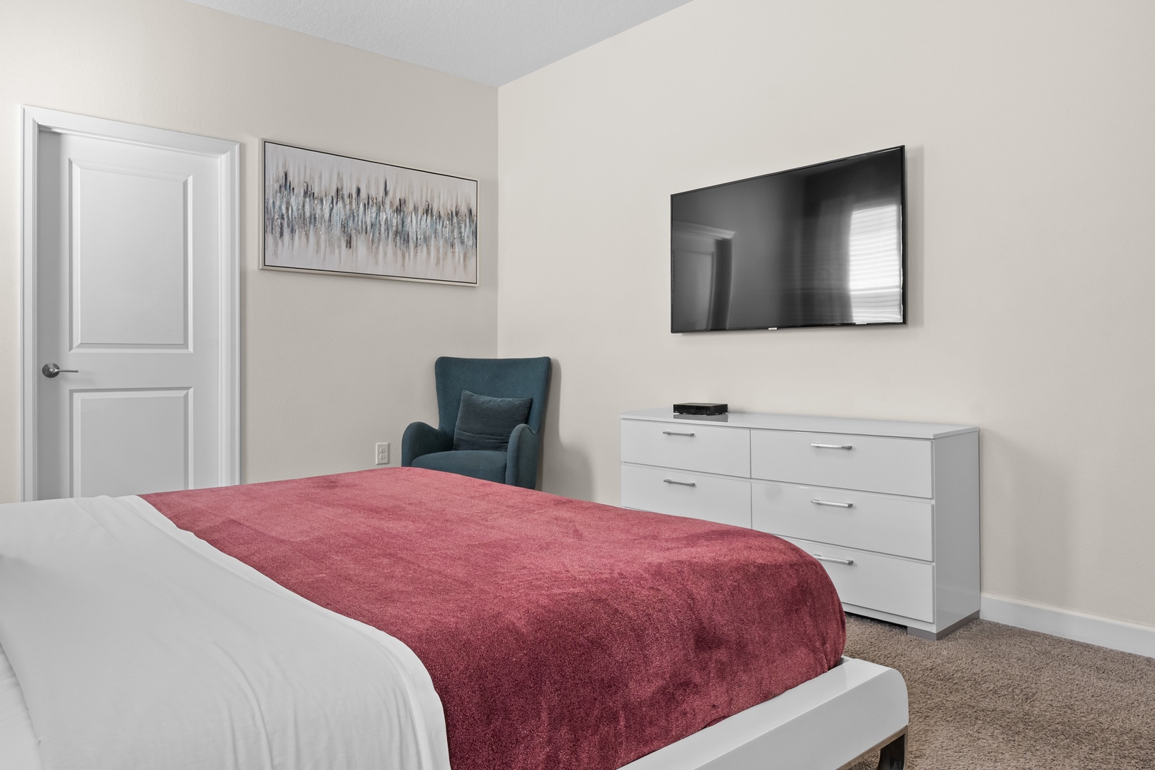 Unwind in your serene bedroom featuring a cozy reading chair, wall-mounted TV, and crisp linens with a vibrant accent throw.