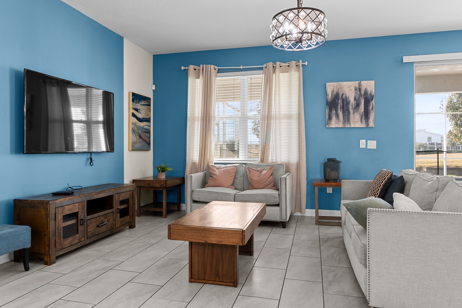 Relax in your bright living room with comfortable seating, modern TV, and beautiful blue accent wall creating a welcoming atmosphere.