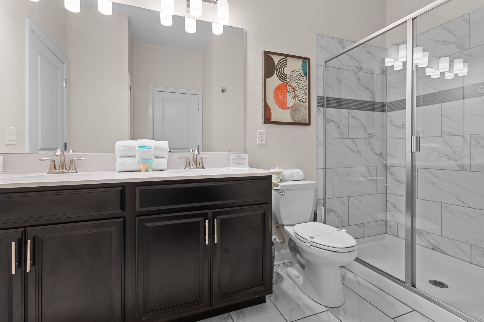 Step into your elegantly designed bathroom featuring luxurious marble-look tiles, dual vanity sinks, and a spacious glass-enclosed shower for ultimate relaxation.