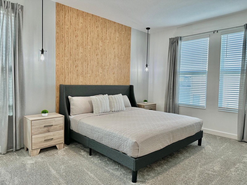 Unwind in your serene bedroom featuring a plush queen bed, warm wood accent wall, and pendant lighting that creates the perfect ambiance for rest.