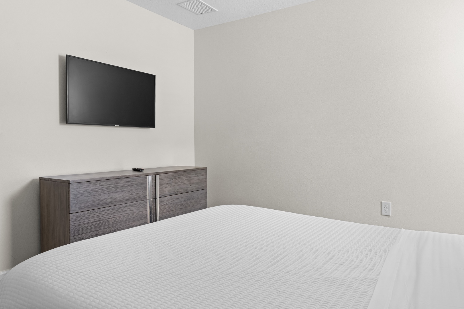 Unwind in your peaceful bedroom with a wall-mounted TV and sleek storage dresser for a comfortable stay.