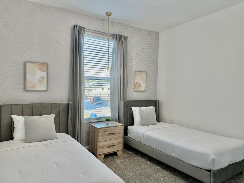 Relax in your stylish twin bedroom with plush bedding, modern furnishings, and serene city views through large windows.