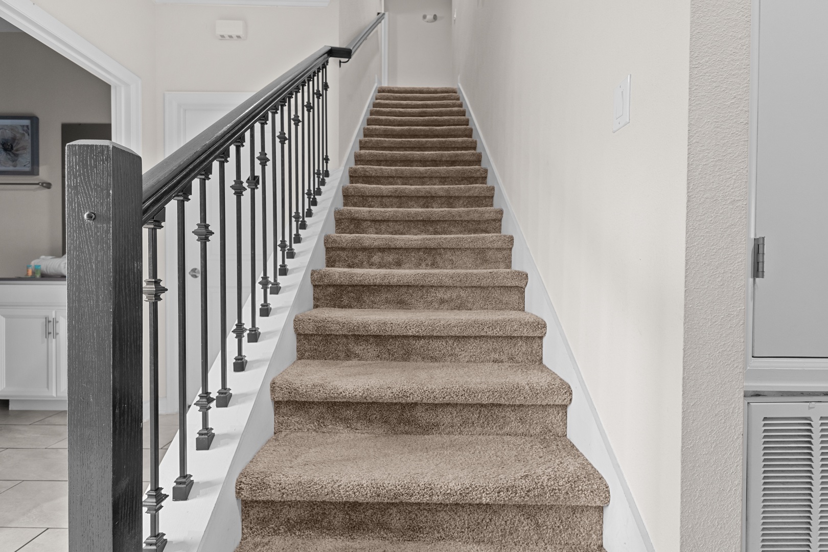 Your journey to the upper level begins with this elegant staircase, featuring plush carpeting and stylish wrought-iron railings for comfort.
