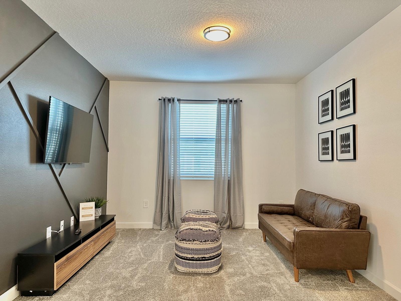 Unwind in your stylish living space with plush leather seating, mounted TV for entertainment, and natural light streaming through your window.