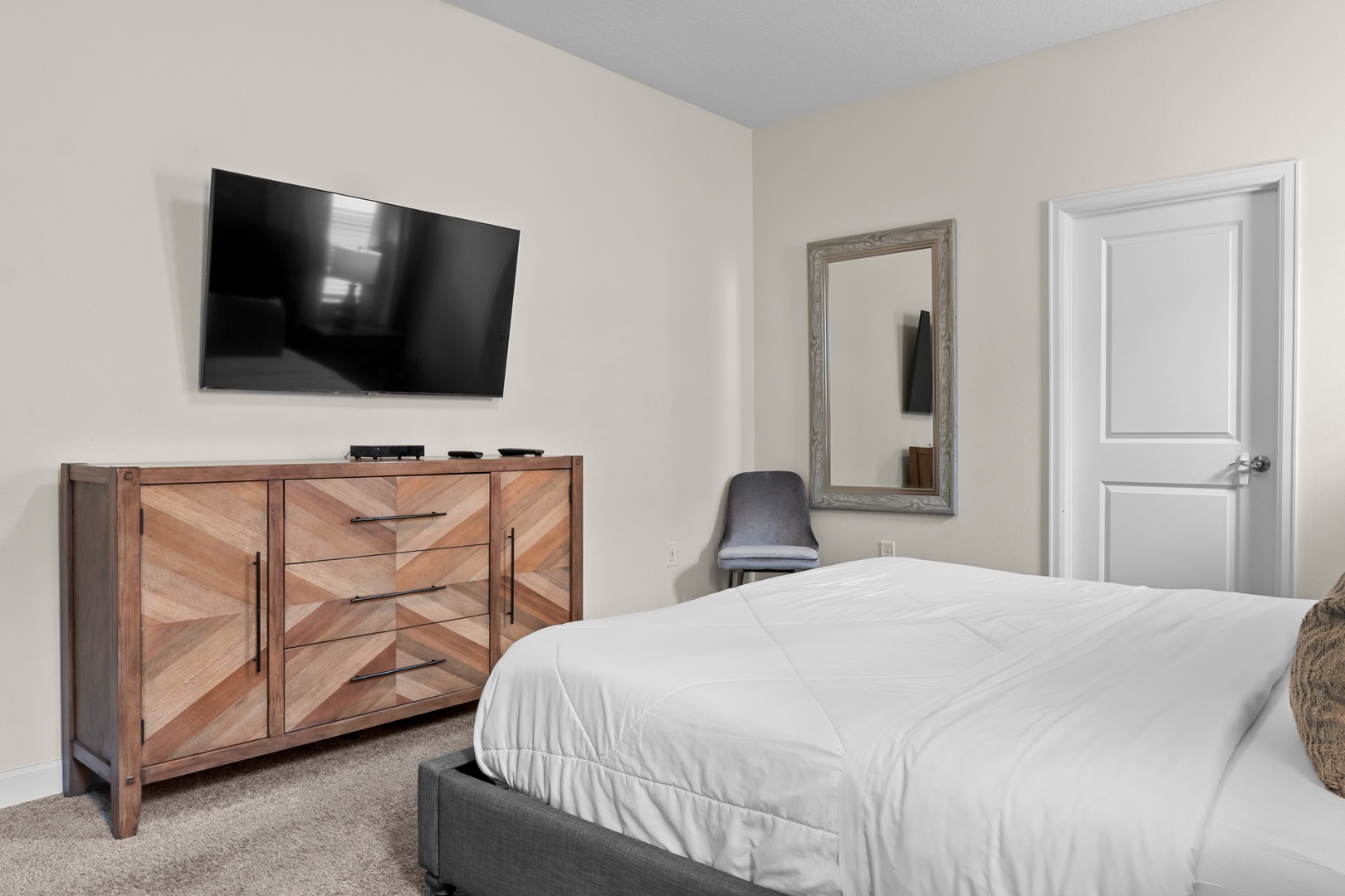 Unwind in your peaceful bedroom featuring a cozy bed, wall-mounted TV for entertainment, and stylish wooden dresser storage.