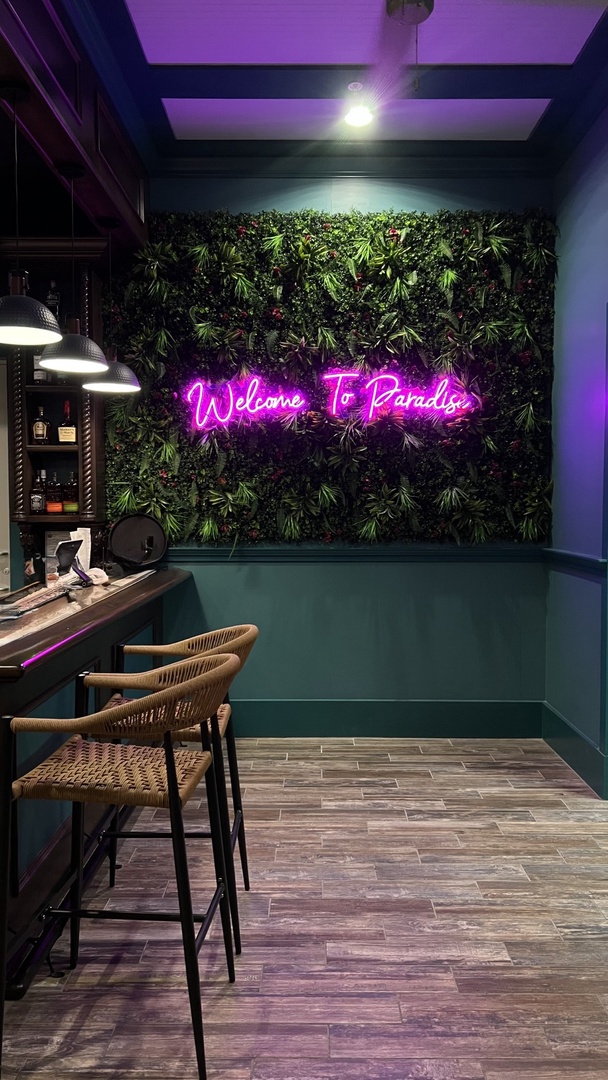 Vibrant neon welcomes you to your tropical paradise, where lush greenery and ambient lighting create your perfect evening escape.