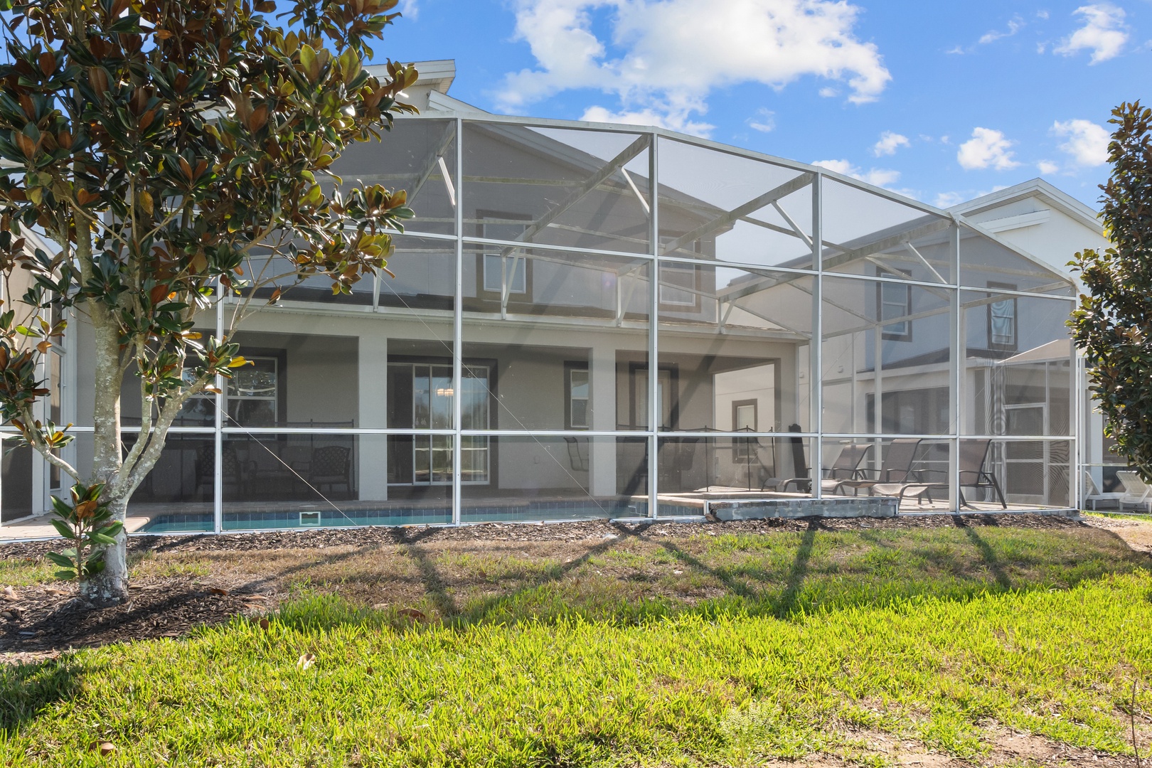 Modern vacation home with screened pool area and tropical landscaping in a quiet residential neighborhood.