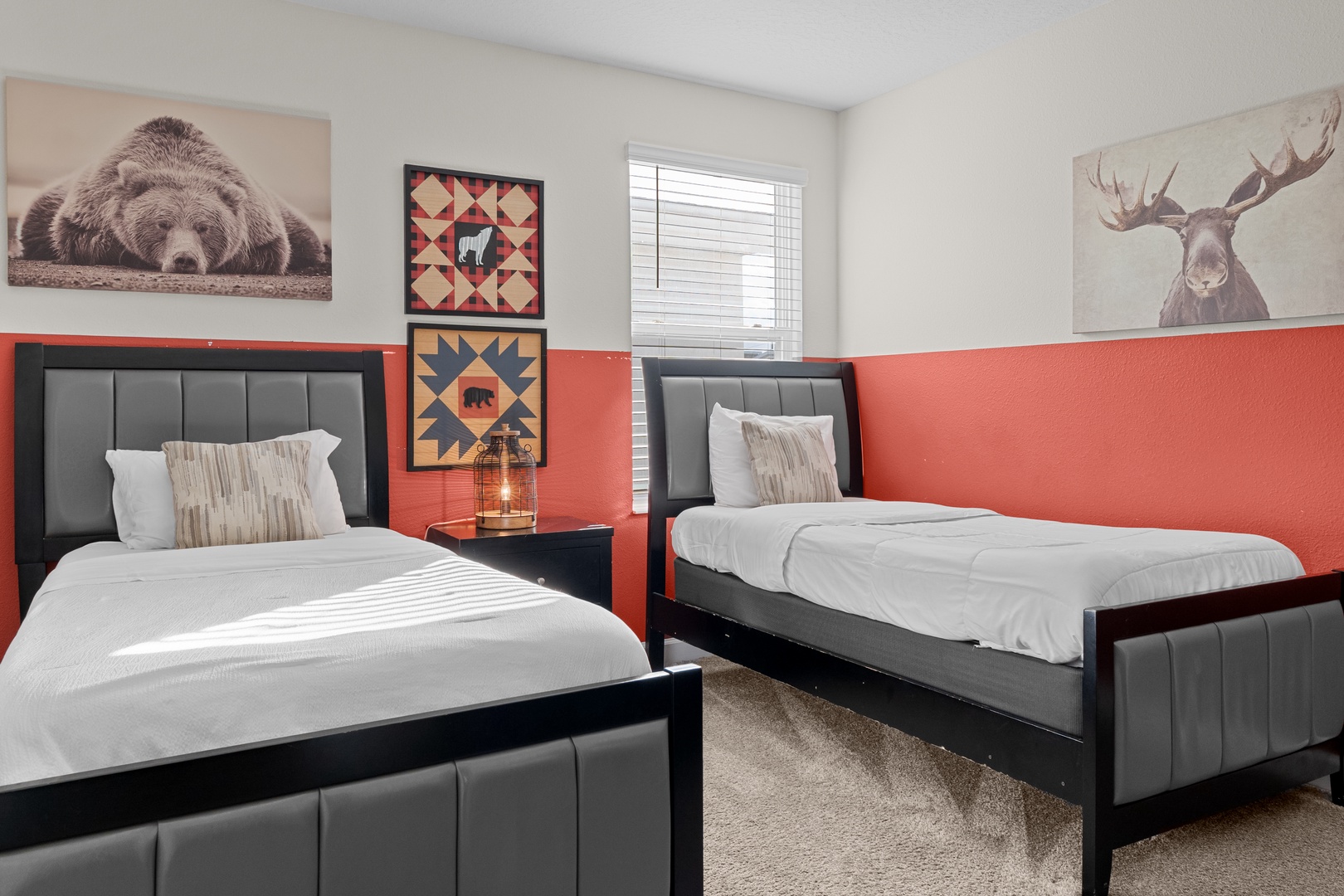 Rest comfortably in twin beds adorned with rustic wildlife art and warm coral walls that create a cozy mountain lodge atmosphere.