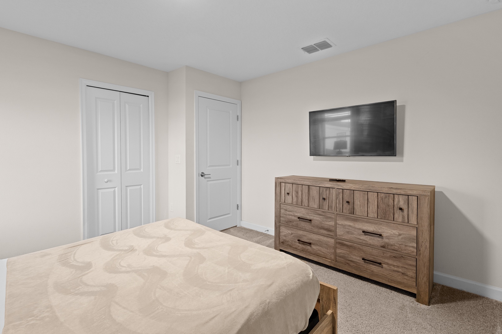 Your comfortable bedroom features a spacious bed, rustic wooden dresser, and wall-mounted TV for relaxing evenings.