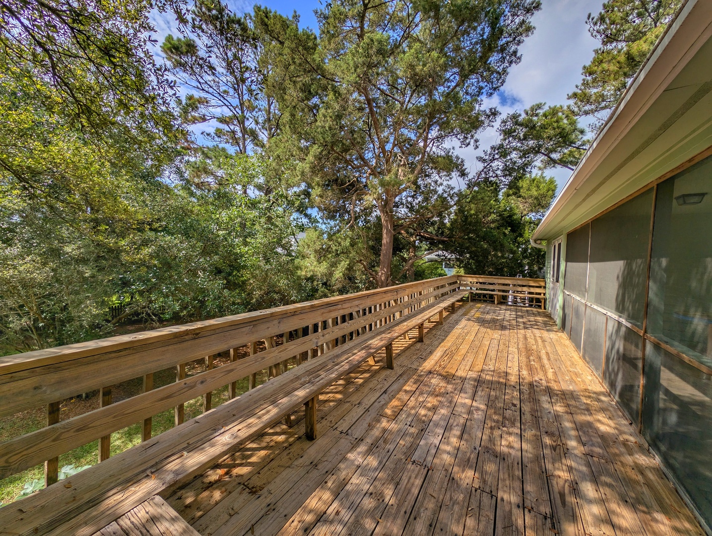 Expansive wooden deck wraps around the property, offering generous outdoor space surrounded by towering pines and lush greenery—perfect for morning coffee or peaceful evenings.