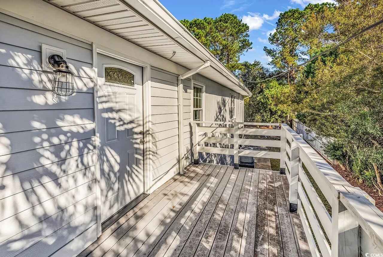 A charming cottage exterior featuring a covered wooden deck surrounded by lush trees and natural landscape.