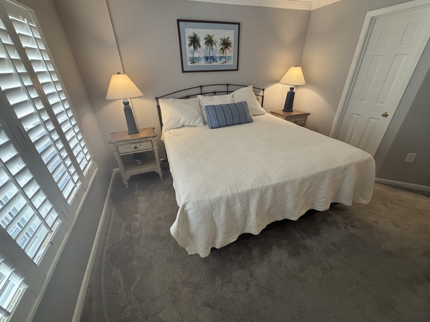 Sink into crisp white linens in your peaceful bedroom retreat, where coastal artwork and soft lamplight create the perfect atmosphere for restful nights.