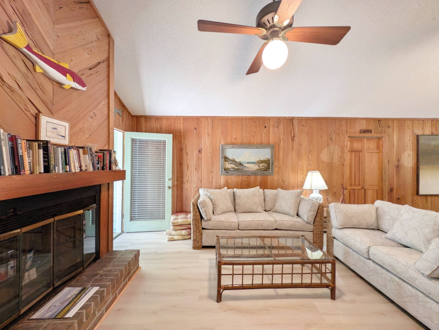 Unwind in your cozy living room with vaulted ceilings, warm wood accents, and plush seating. A fireplace adds charm while beach art sets a coastal vibe for your perfect getaway.