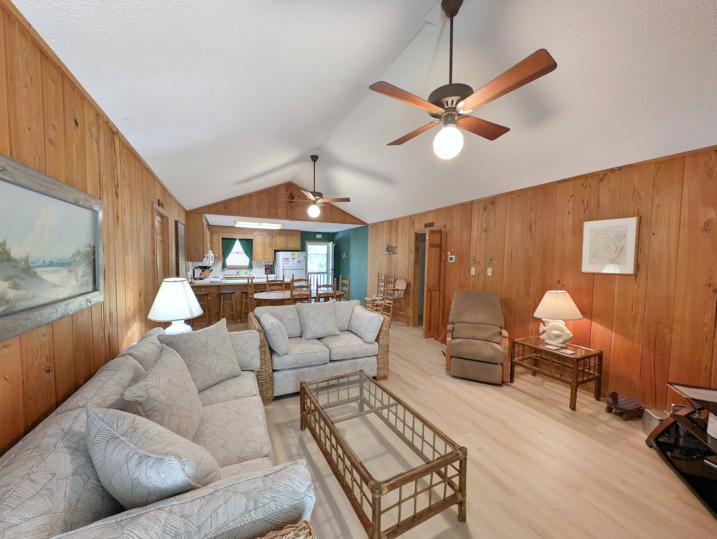 Relax in this spacious, open-concept living area with vaulted ceilings and warm wood paneling. Cozy seating, ceiling fans, and coastal charm create your perfect retreat.