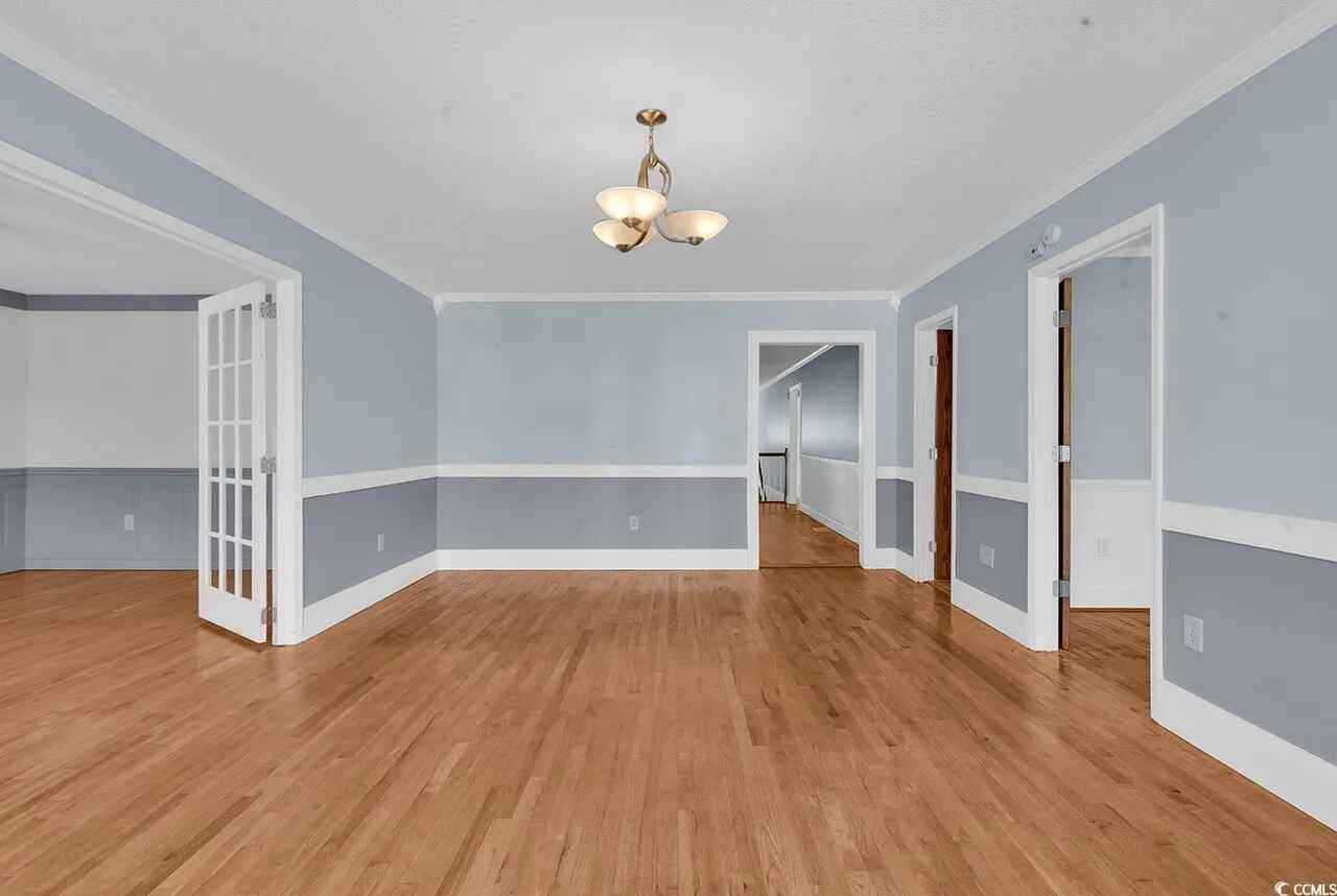Elegant open-concept living space with gleaming hardwood floors, soothing blue-gray walls, and classic white crown molding creating a welcoming atmosphere for your stay.