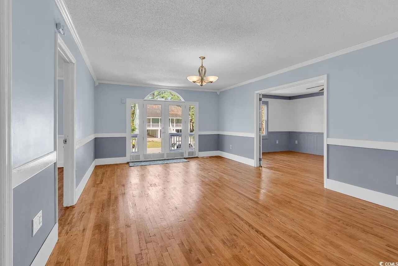 Step into your elegant dining space featuring beautiful hardwood floors, soft blue walls, and French doors opening to outdoor views.