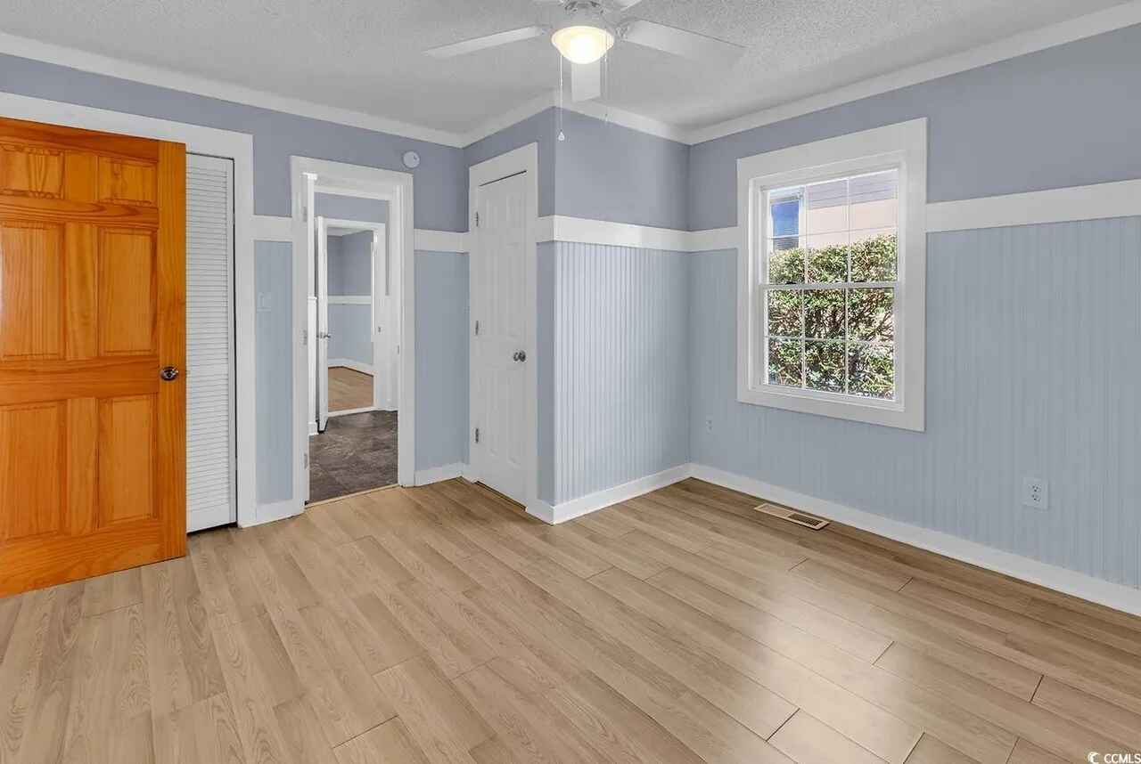 Your bright room features charming blue walls with white trim, gleaming hardwood floors, and a window overlooking greenery outside.
