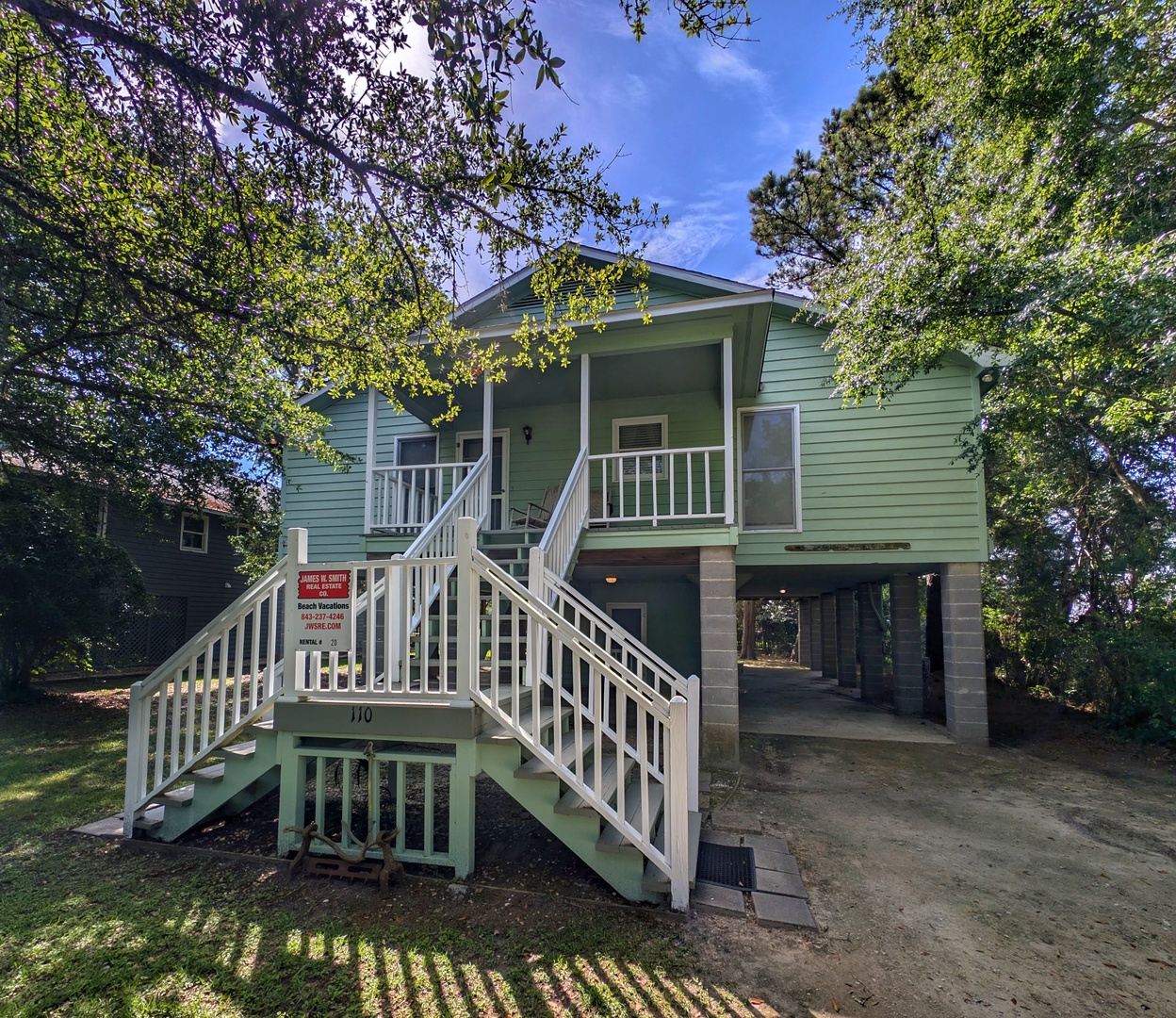 This charming coastal cottage sits nestled among mature trees in a peaceful residential setting. The property features covered front porch access, ground-level parking, and a welcoming exterior ideal for a relaxing beach getaway.