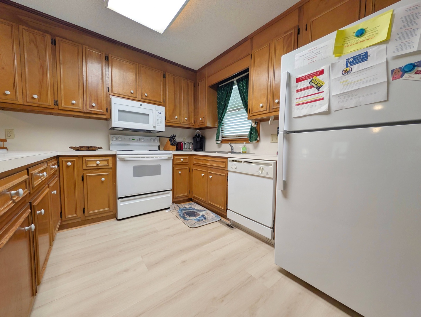 Step into your fully equipped kitchen with everything you need for a comfortable stay: microwave, dishwasher, oven, and warm wood cabinetry lit by natural skylight glow.