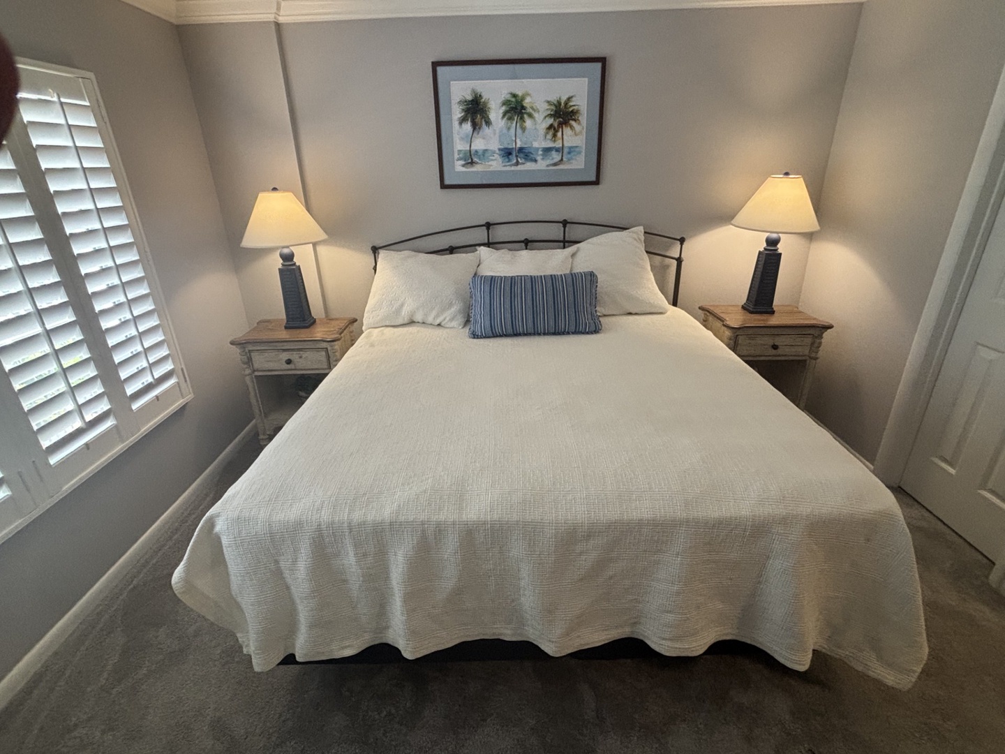 Sink into crisp white linens in your peaceful bedroom retreat, where tropical artwork and soft bedside lighting create the perfect atmosphere.
