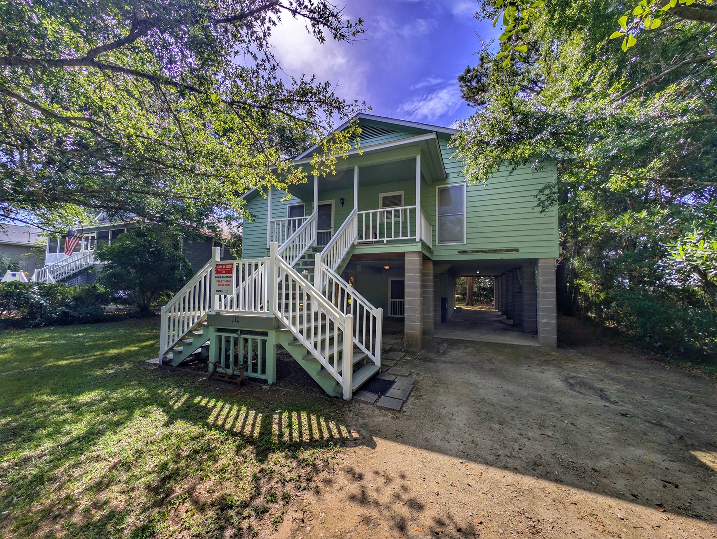 Charming coastal-style beach house nestled among mature trees with covered parking and welcoming front porch in a peaceful neighborhood setting.