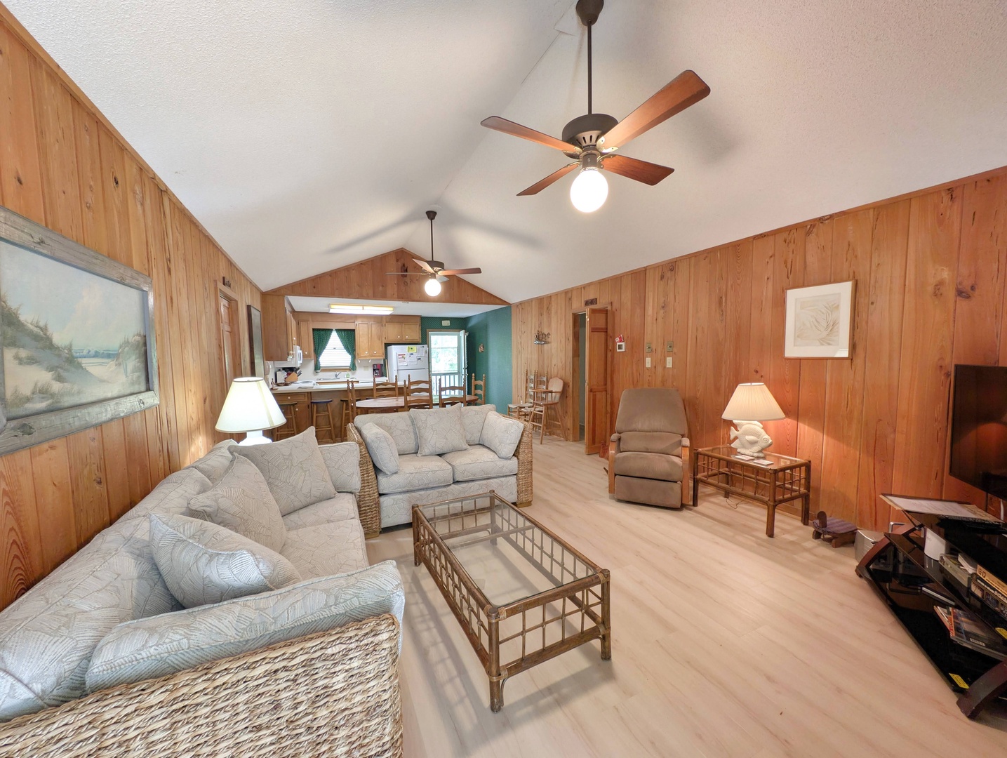 Relax in your spacious open living area with vaulted ceilings and warm wood paneling. Cozy seating invites you to unwind while ceiling fans keep the space comfortable.