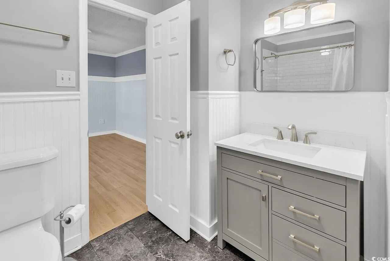 Step into your pristine bathroom featuring elegant gray vanity, marble countertops, and classic white wainscoting for a refined, spa-like experience.