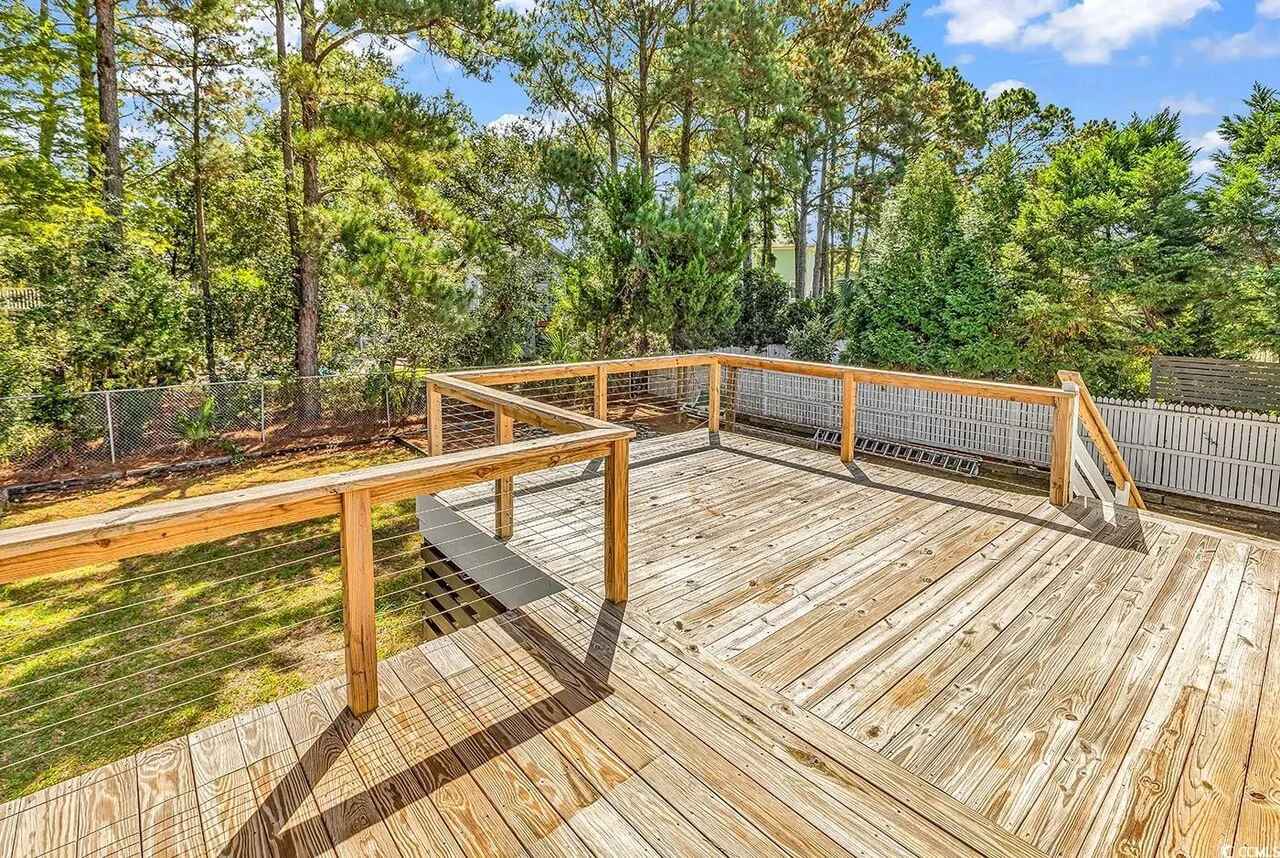 Spacious wooden deck overlooks lush forest surroundings, providing a peaceful outdoor retreat for relaxation and gatherings.