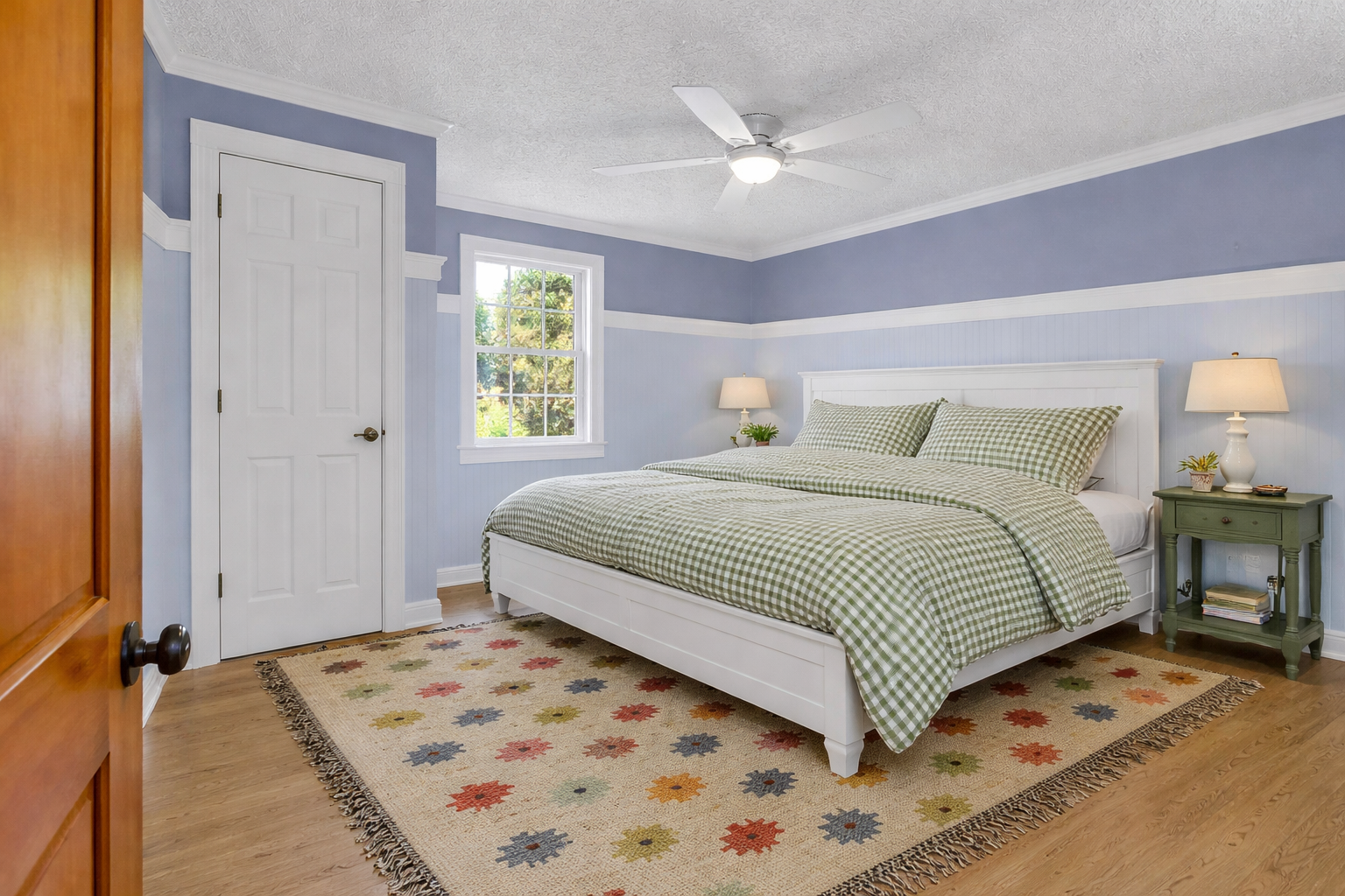 Sink into comfort in your peaceful bedroom featuring soft blue walls, cozy gingham bedding, and natural light streaming through the window.