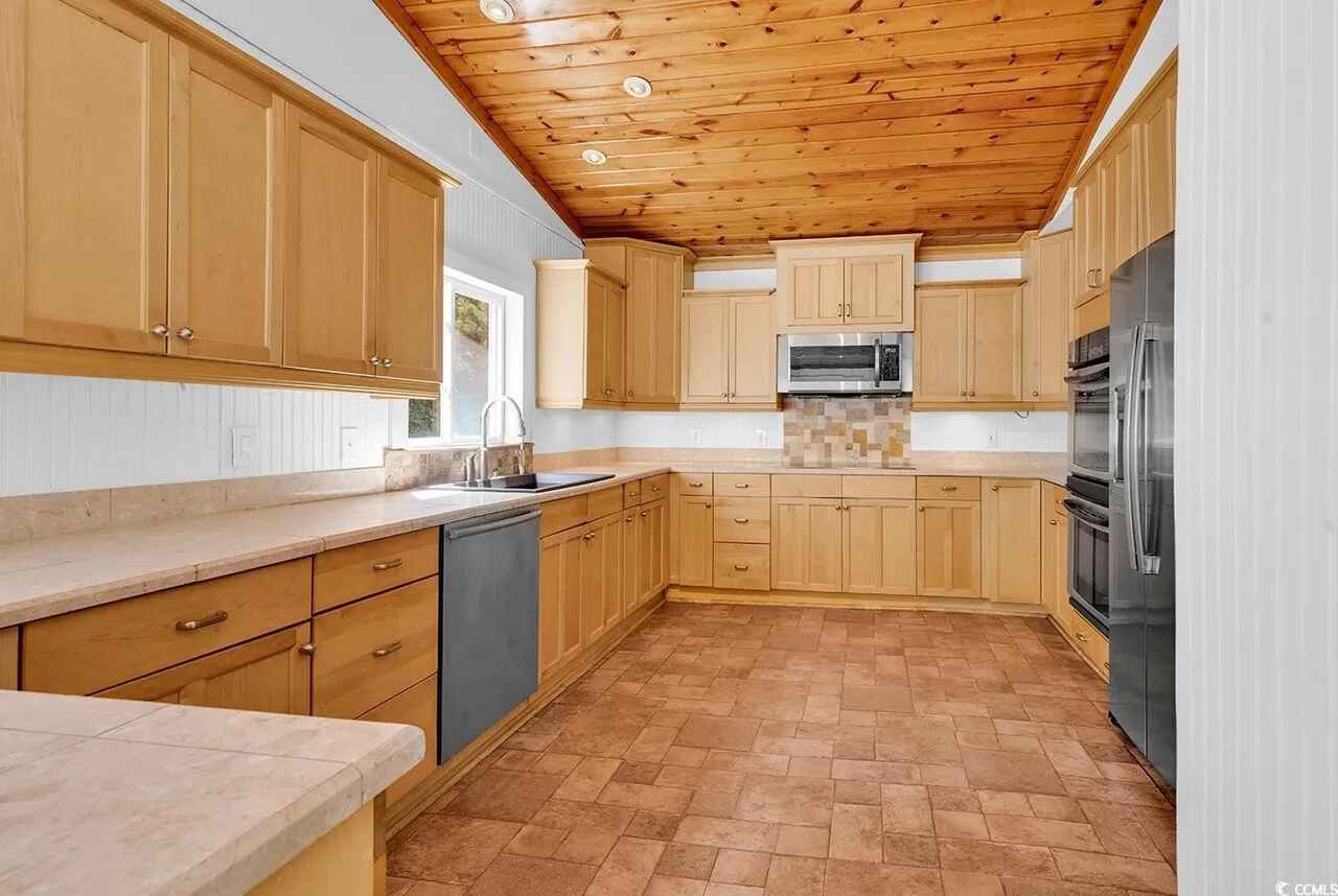 Your spacious kitchen features warm wood cabinets, granite counters, and modern appliances under beautiful exposed wood ceiling beams.