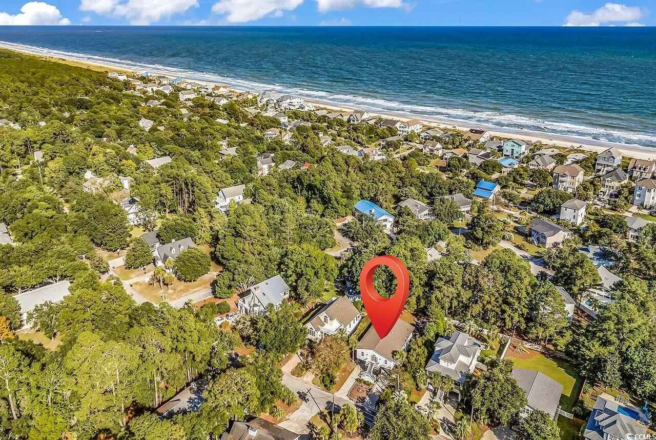 Aerial view of a charming beach community nestled among lush trees, with the property conveniently located just moments from pristine sandy shores.