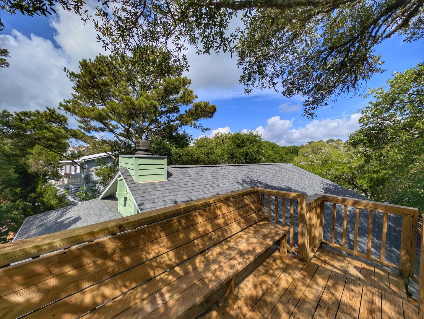 Spacious wooden deck surrounded by lush trees and blue skies, perfect for morning coffee or relaxing under dappled sunlight with nature at your doorstep.