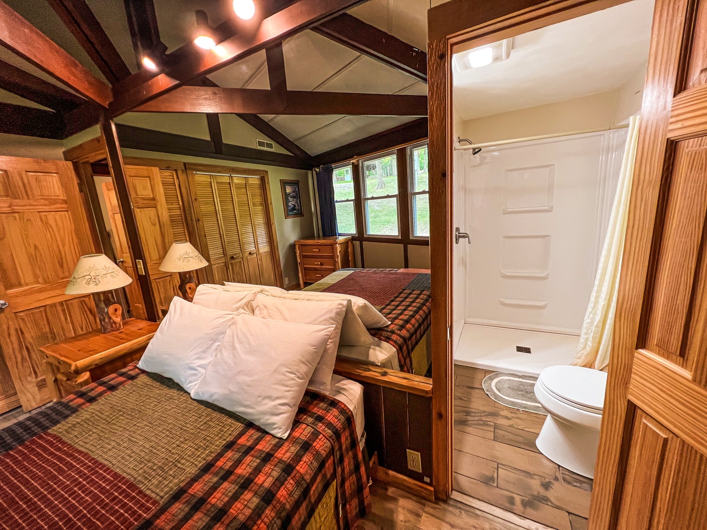 Settle into your cozy cabin retreat with charming wooden beams overhead, plaid-covered beds, and a private ensuite bathroom—everything you need for a peaceful getaway.