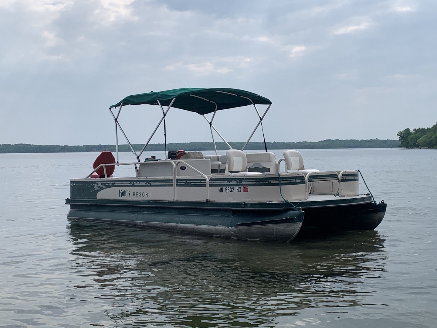 A pontoon boat floats on calm lake waters, ready for leisurely cruises and lake adventures surrounded by scenic wooded shorelines.