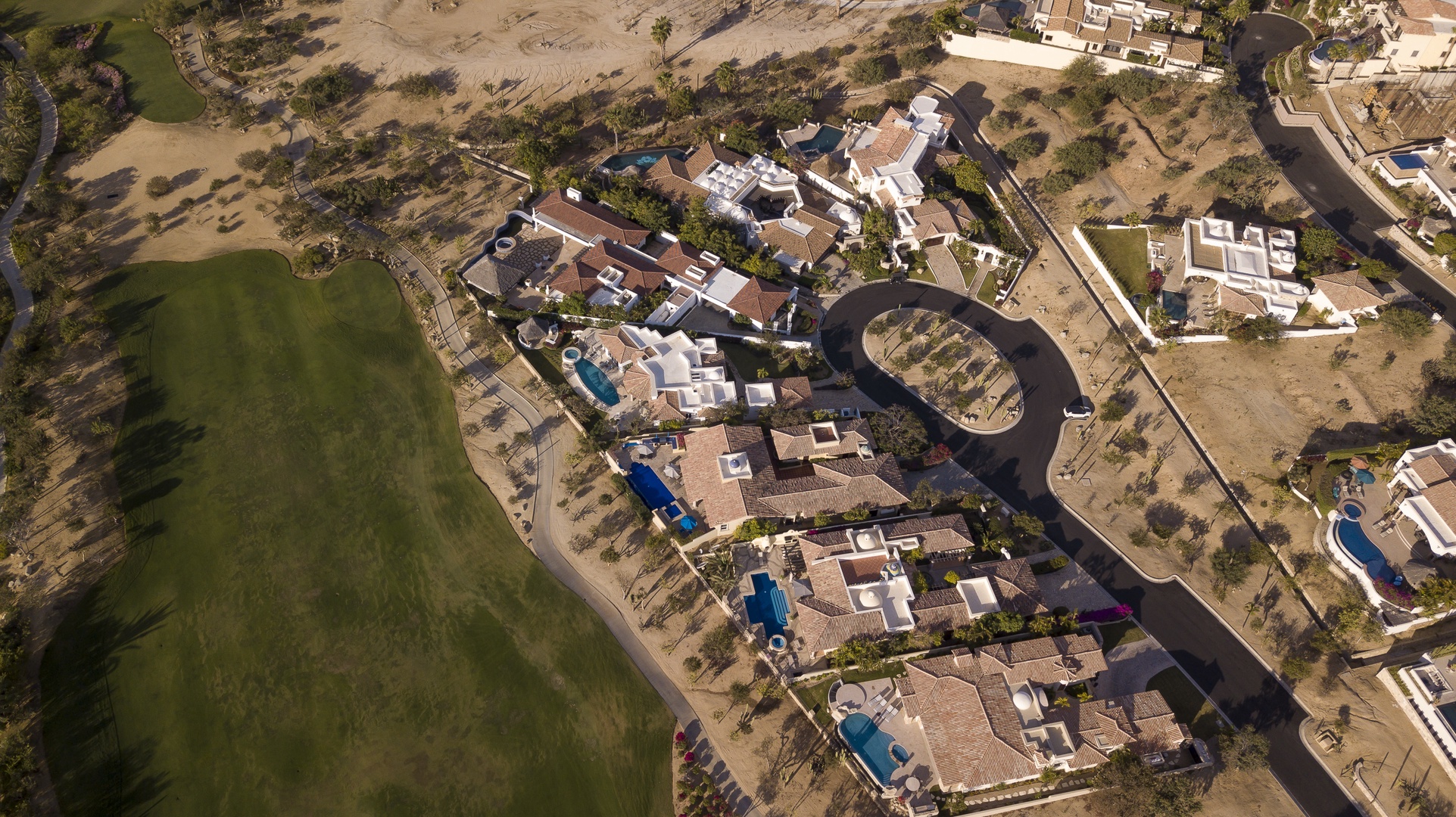 Aerial view of an upscale residential development featuring luxury villas with private pools arranged along curved streets.