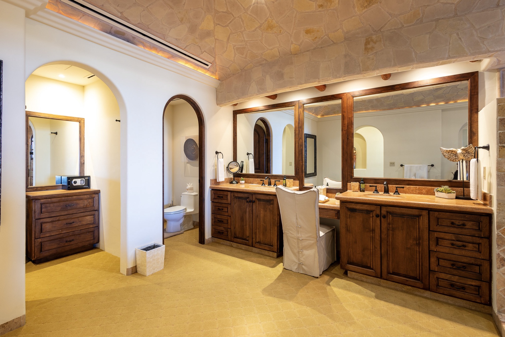 Step into your private sanctuary with vaulted stone ceilings, dual vanities in rich wood, and abundant natural light through the skylight above.