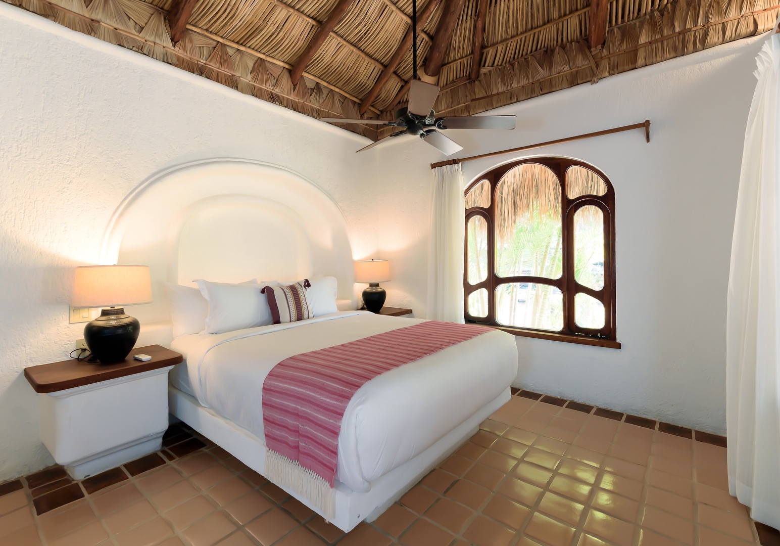 Drift off beneath a charming palapa ceiling in your serene bedroom, where crisp linens and warm tile floors create a peaceful tropical retreat.