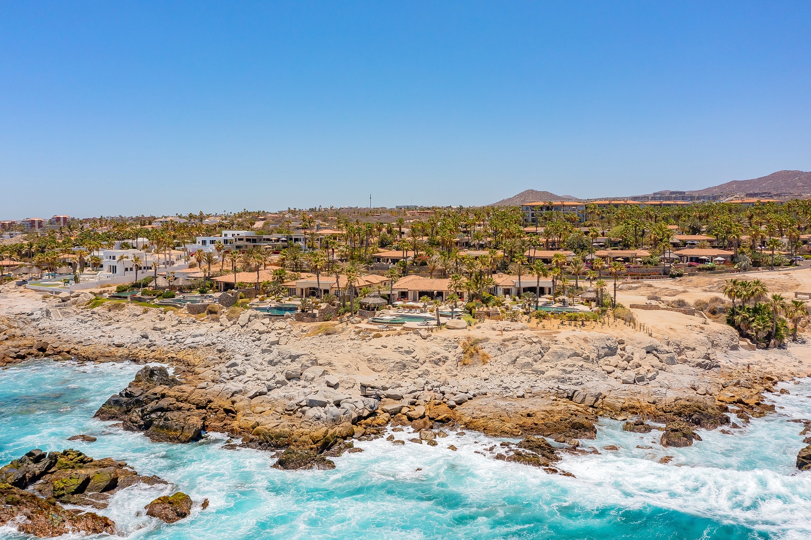Stunning coastal resort community with turquoise waters, rocky shoreline, and mountains creating a perfect tropical getaway backdrop.