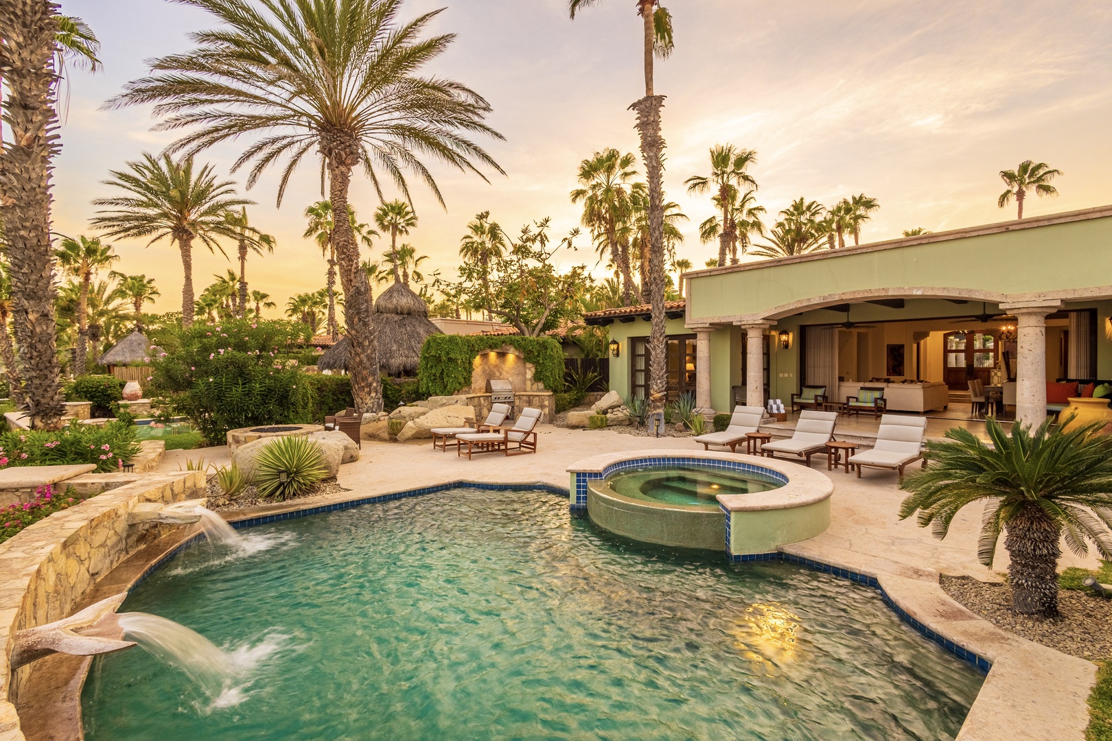 Tropical oasis with sparkling pool, elevated hot tub, and lush desert landscaping. Lounge by the water's edge as golden hour light bathes the private patio, then retreat indoors through the arched entryway.