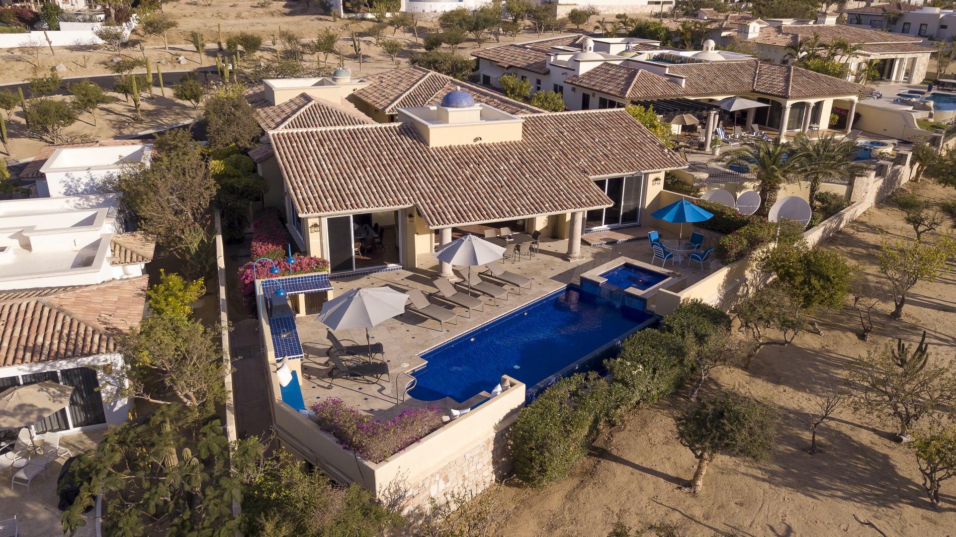 Stunning aerial view of a luxury desert villa featuring a sparkling blue pool, elegant terrace, and traditional tile roofing.