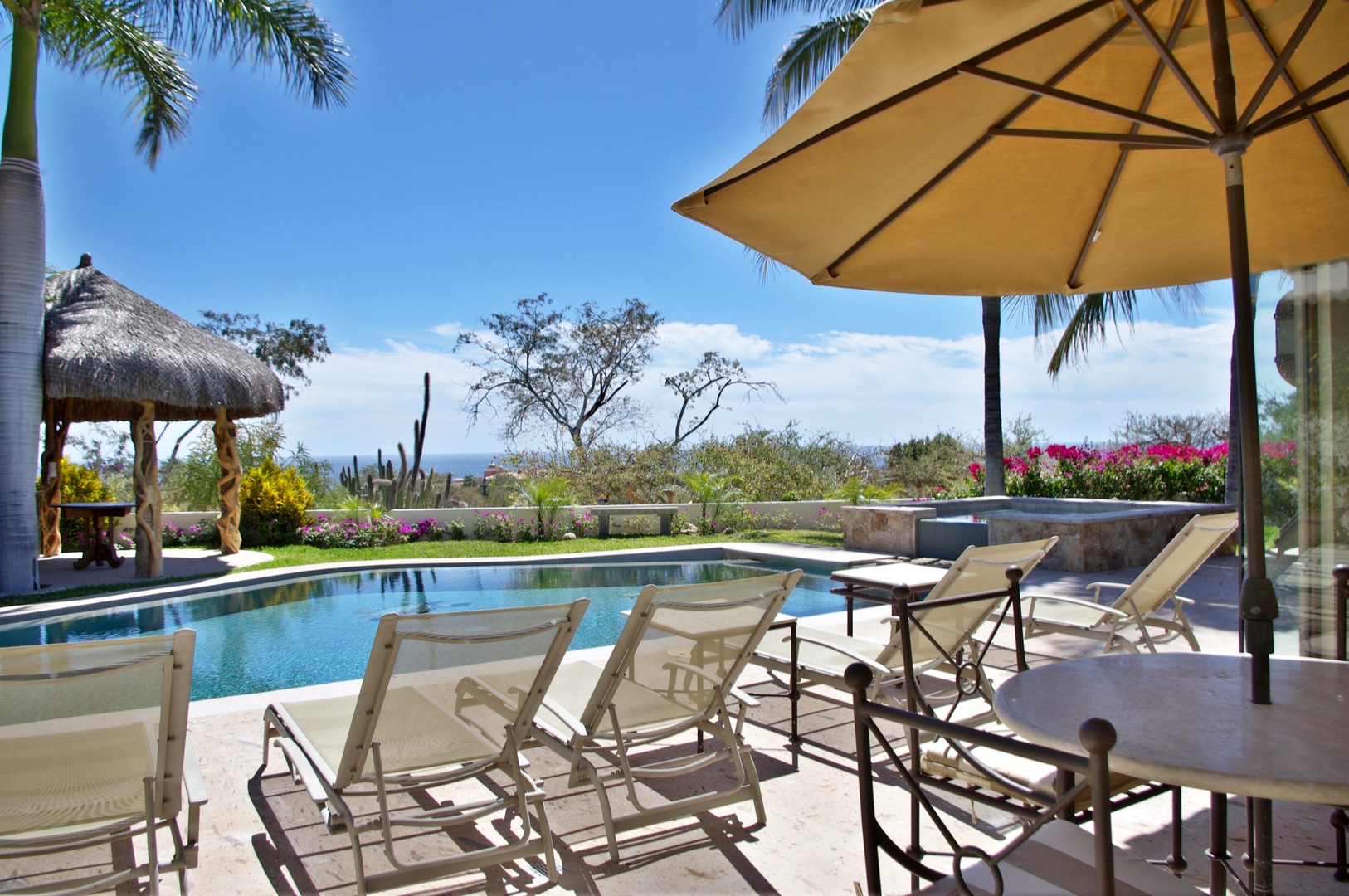 Stretch out poolside under swaying palms with ocean views in the distance. Lounge chairs, shade, and a peaceful desert-meets-tropics escape await.